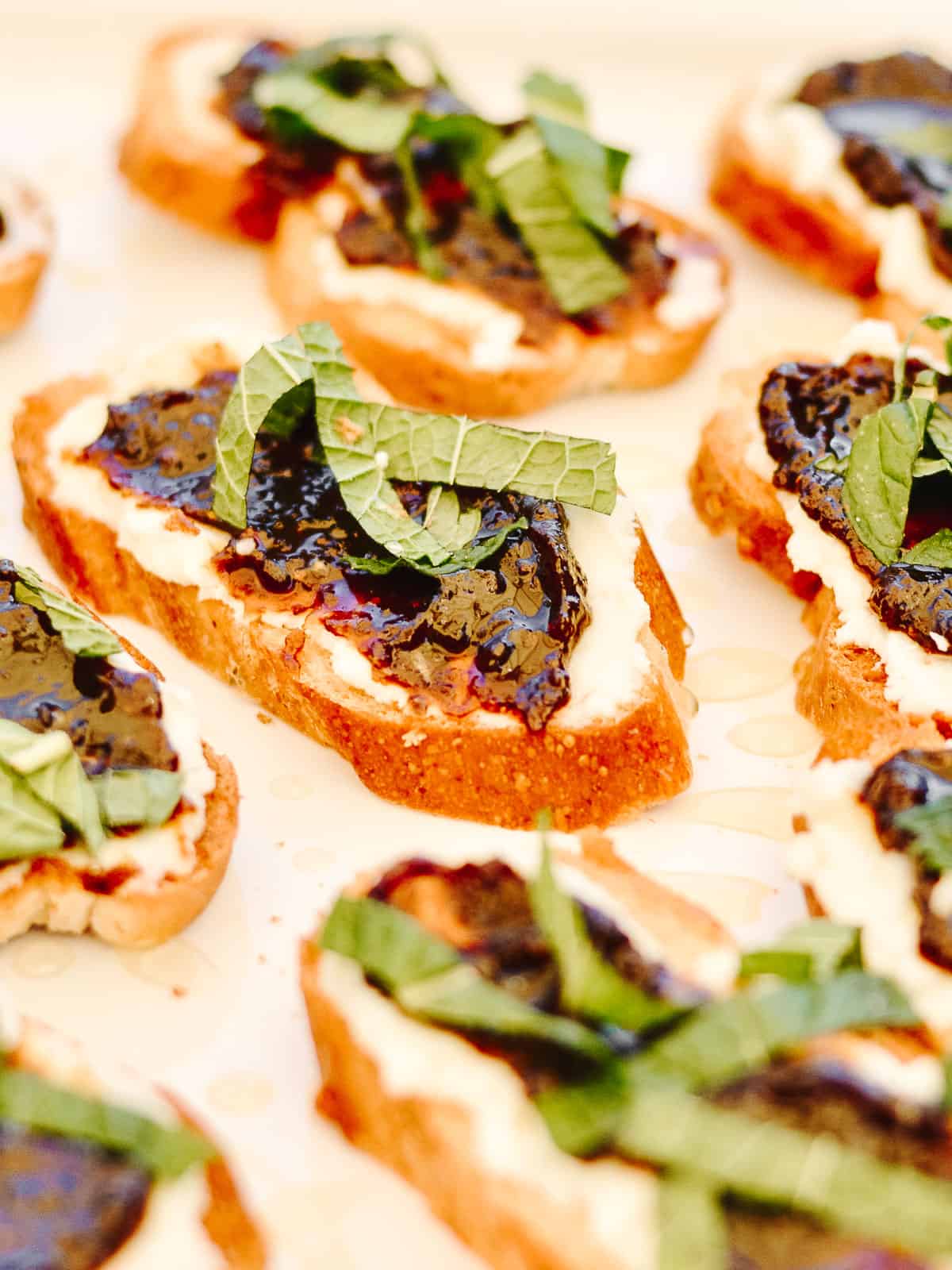 Goat cheese on top of bread slices with fig jam and sliced mint leaves.