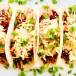 Overhead view of four Korean BBQ tacos laying on a white plate.