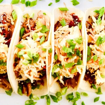 Overhead view of four Korean BBQ tacos laying on a white plate.