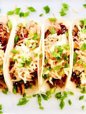 Overhead view of four Korean BBQ tacos laying on a white plate.