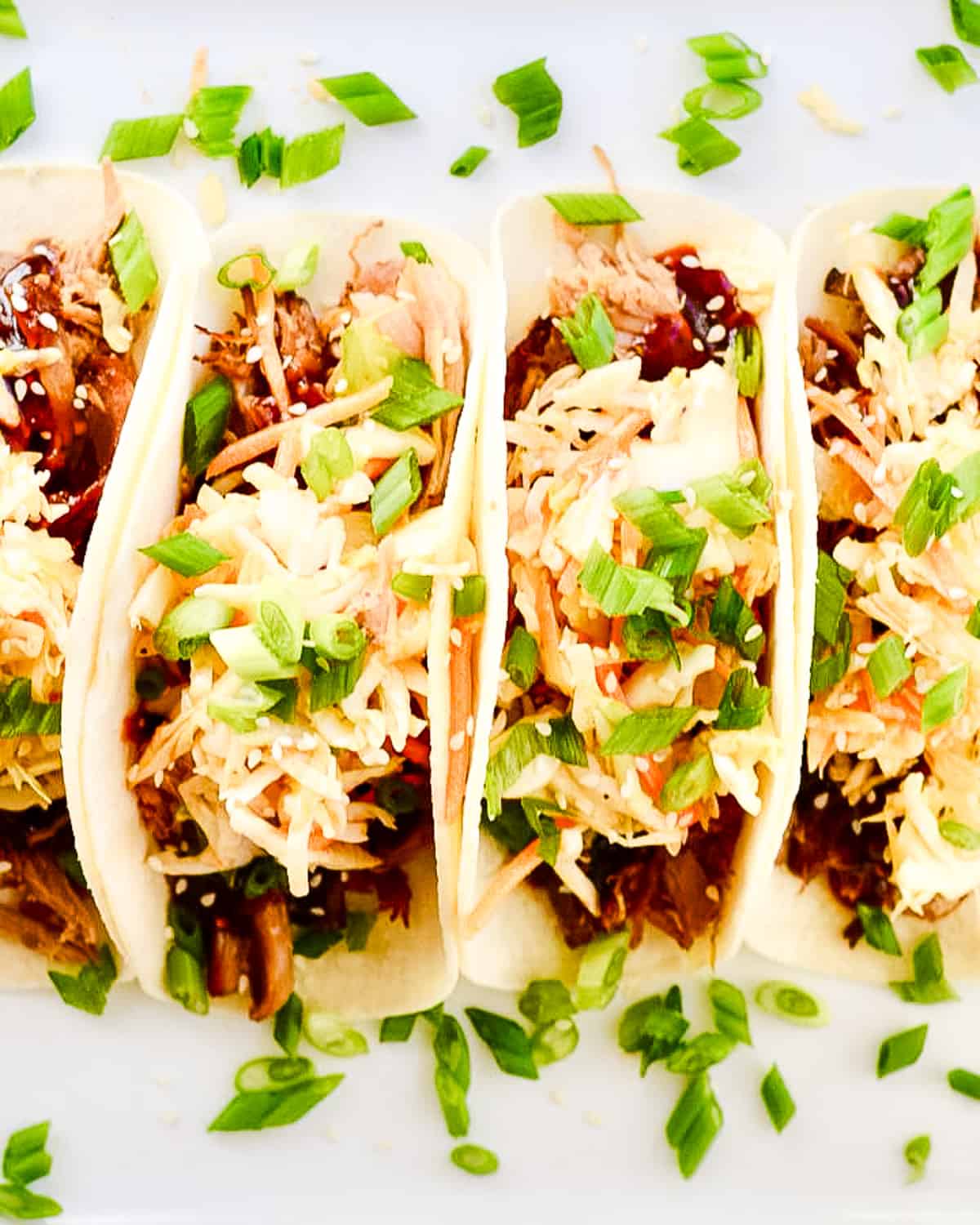 Overhead view of four Korean BBQ tacos laying on a white plate.