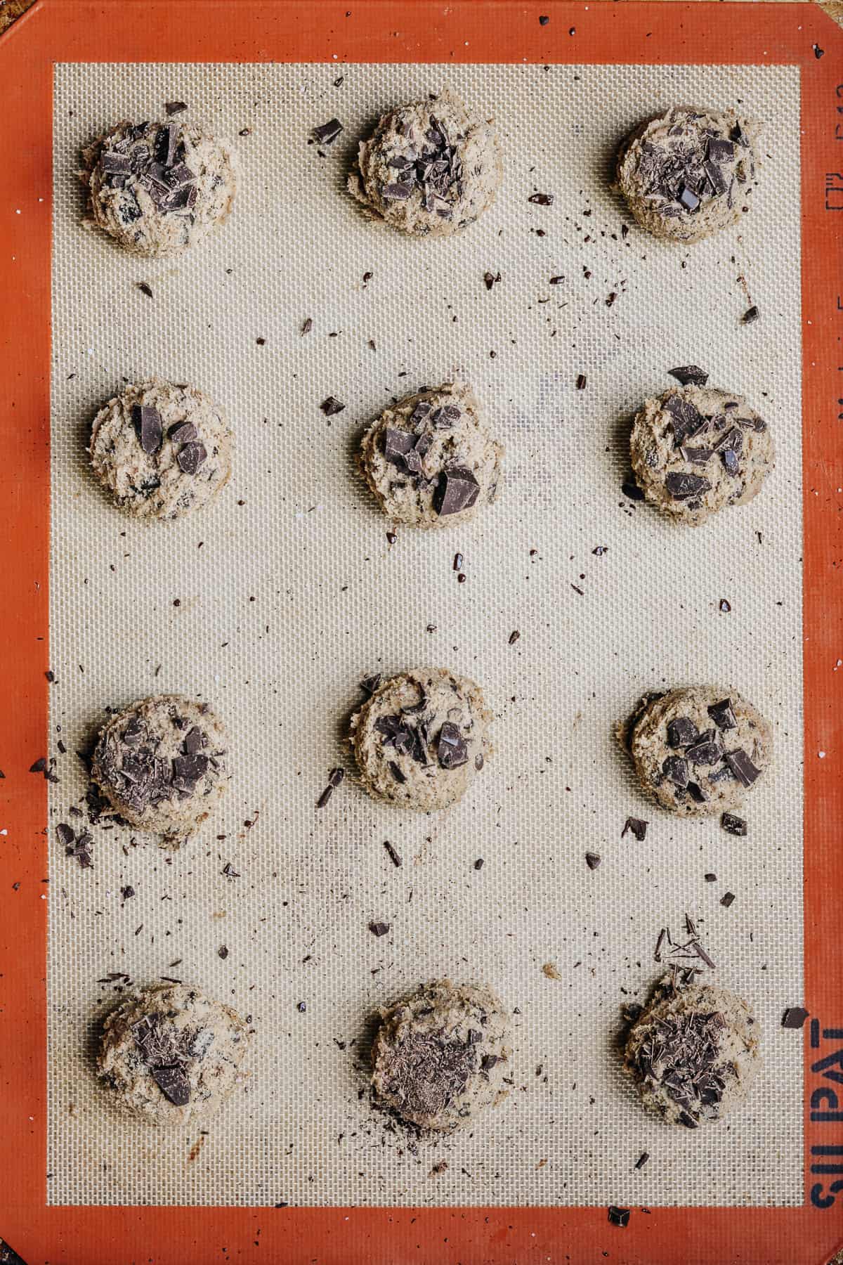 Scooped cookie dough on silpat mat on a baking sheet.