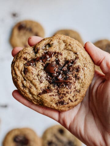 Hand holding an espresso cookie with more cookies in background.
