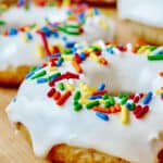Close up of vanilla donut with white frosting and sprinkles.