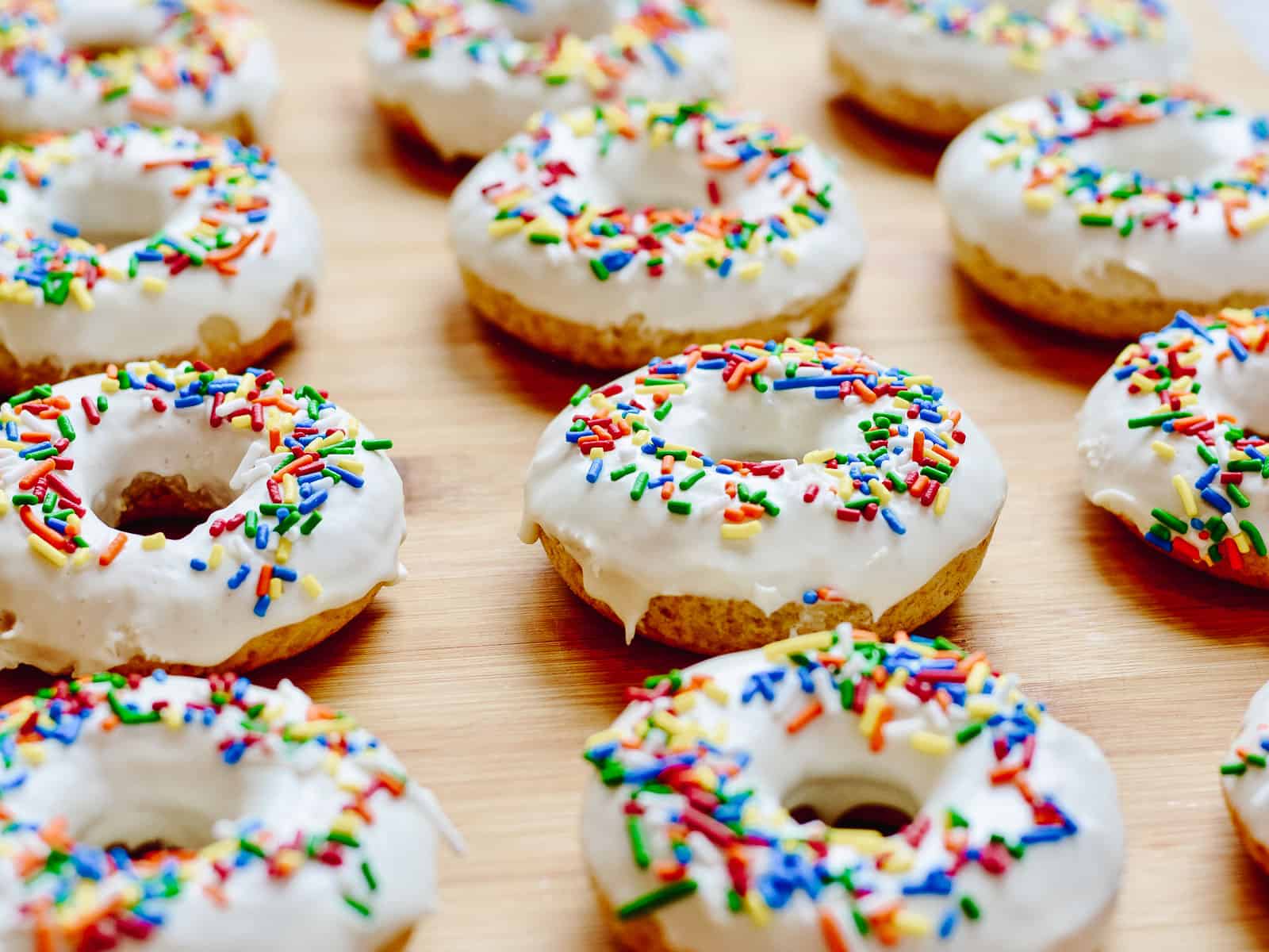 Donuts lined up in a row with vanilla frosting and sprinkles.