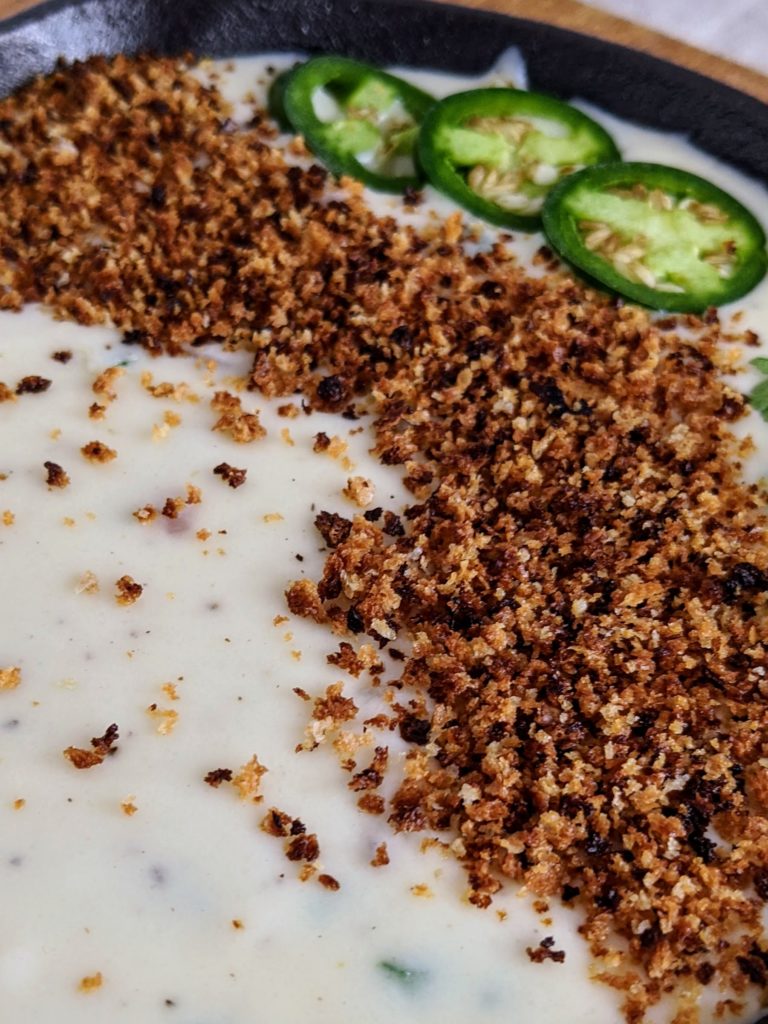 The BEST queso dip with jalapeño, red onion, monterey jack cheese. Topped with bread crumbs, jalapeños and cilantro. Seriously the most amazing queso ever.