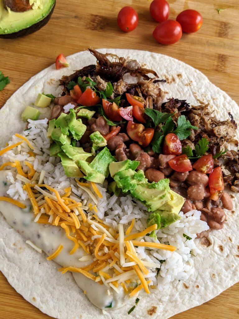 Carnitas burrito with queso, jalapeño pinto beans, and all the fixings! So delicious and easy to make ahead and freeze for another lunch or dinner.