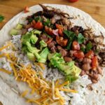 Carnitas burrito with queso, jalapeño pinto beans, and all the fixings! So delicious and easy to make ahead and freeze for another lunch or dinner.