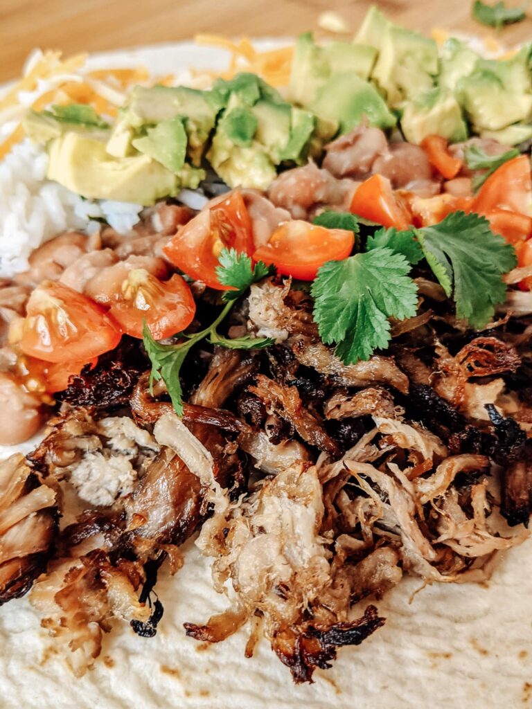 Carnitas burrito with queso, jalapeño pinto beans, and all the fixings! So delicious and easy to make ahead and freeze for another lunch or dinner.