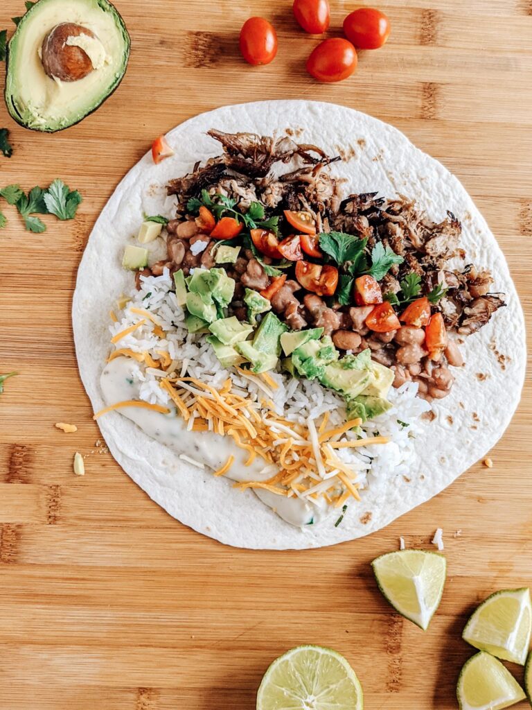 Carnitas burrito with queso, jalapeño pinto beans, and all the fixings! So delicious and easy to make ahead and freeze for another lunch or dinner.