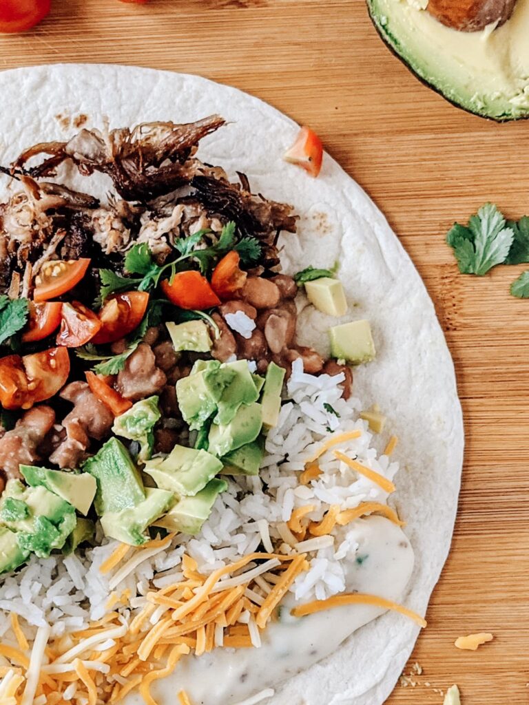 Carnitas burrito with queso, jalapeño pinto beans, and all the fixings! So delicious and easy to make ahead and freeze for another lunch or dinner.