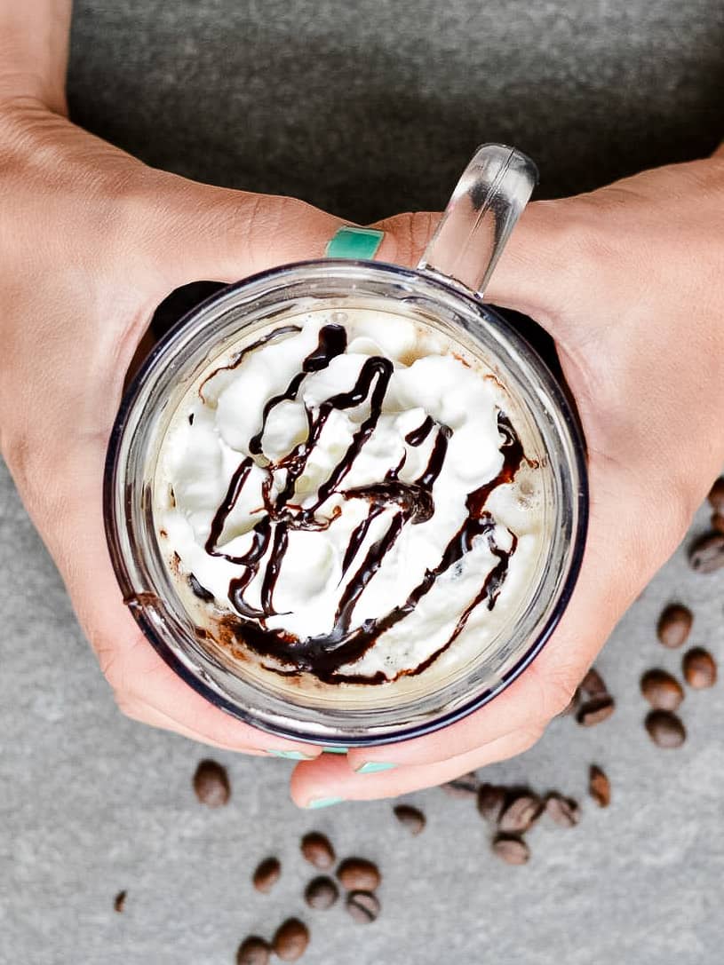 Hans wrapped around a glass mug of irish cream mocha with whipped cream and chocolate drizzle.