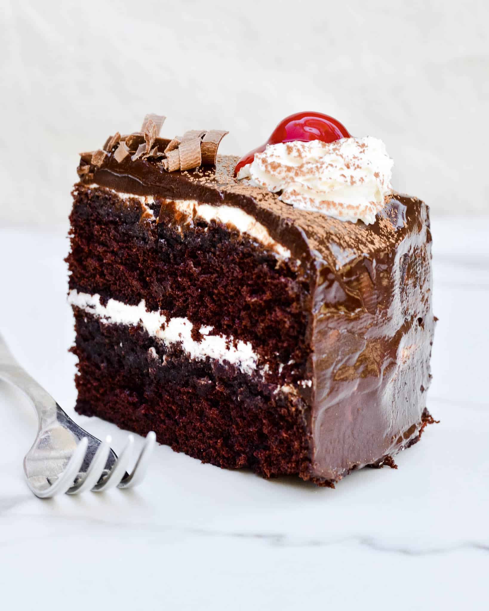 Slice of black forest cake with fork. Chocolate ganache and cherry on top with whip cream.