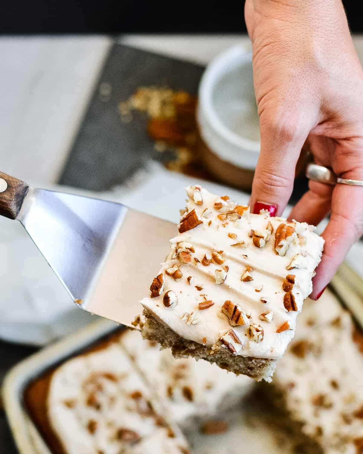 Hand serving a slice of pecan cake with the rest of the cake in the background.