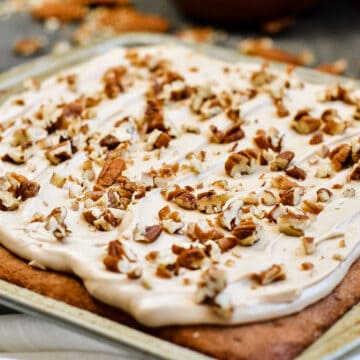 Up close of pecan cake with maple frosting, pecans sprinkled on top.