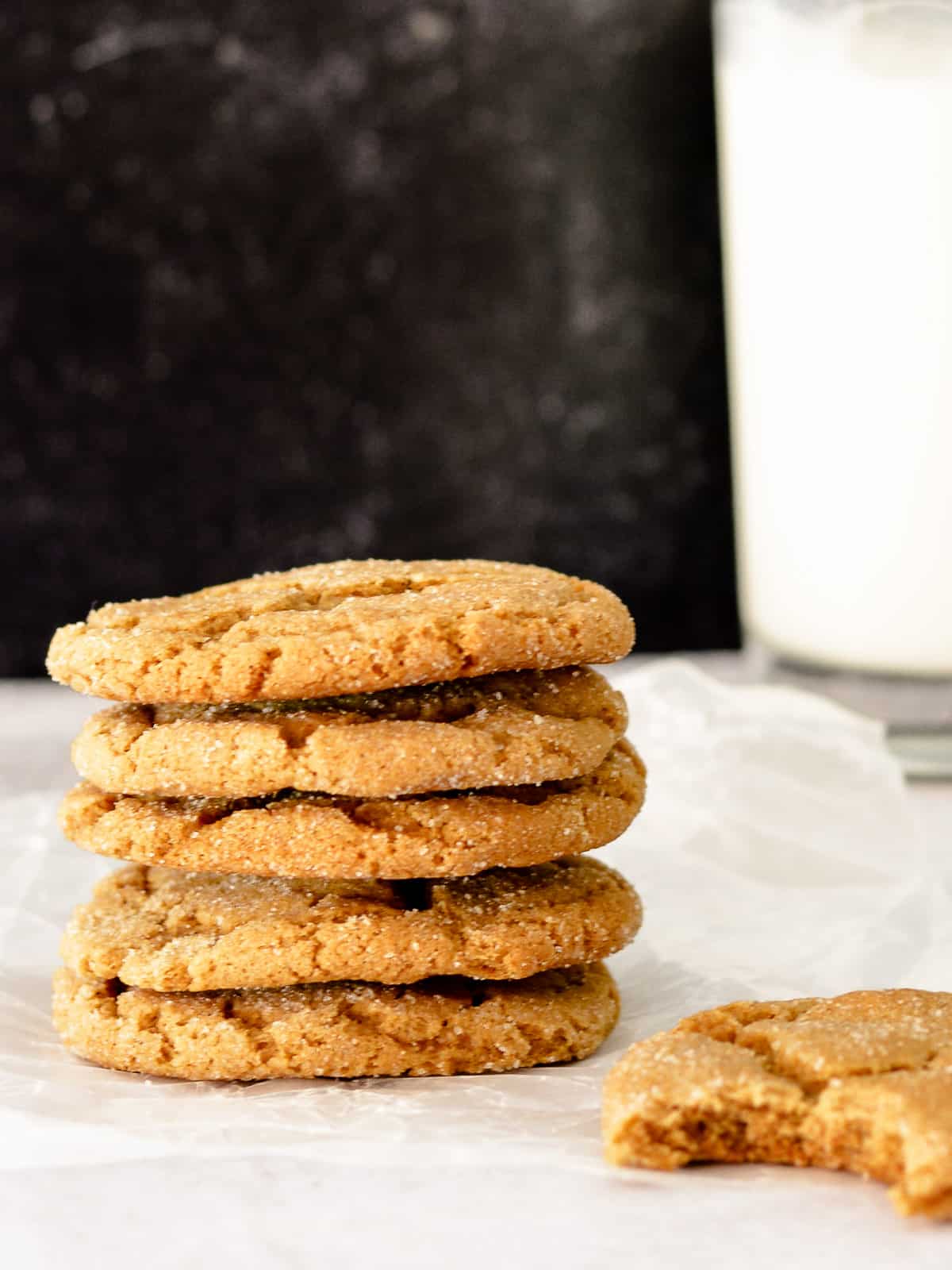 Stack of ginger molasses cookies with glass of milk in background.