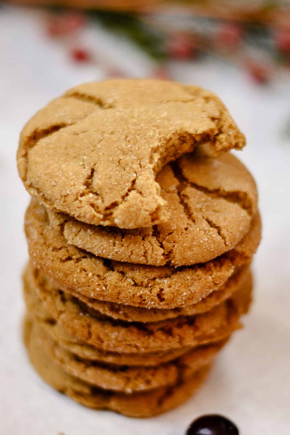Stack of molasses cookies with bite out of top cookie. Sprig of holly in background.
