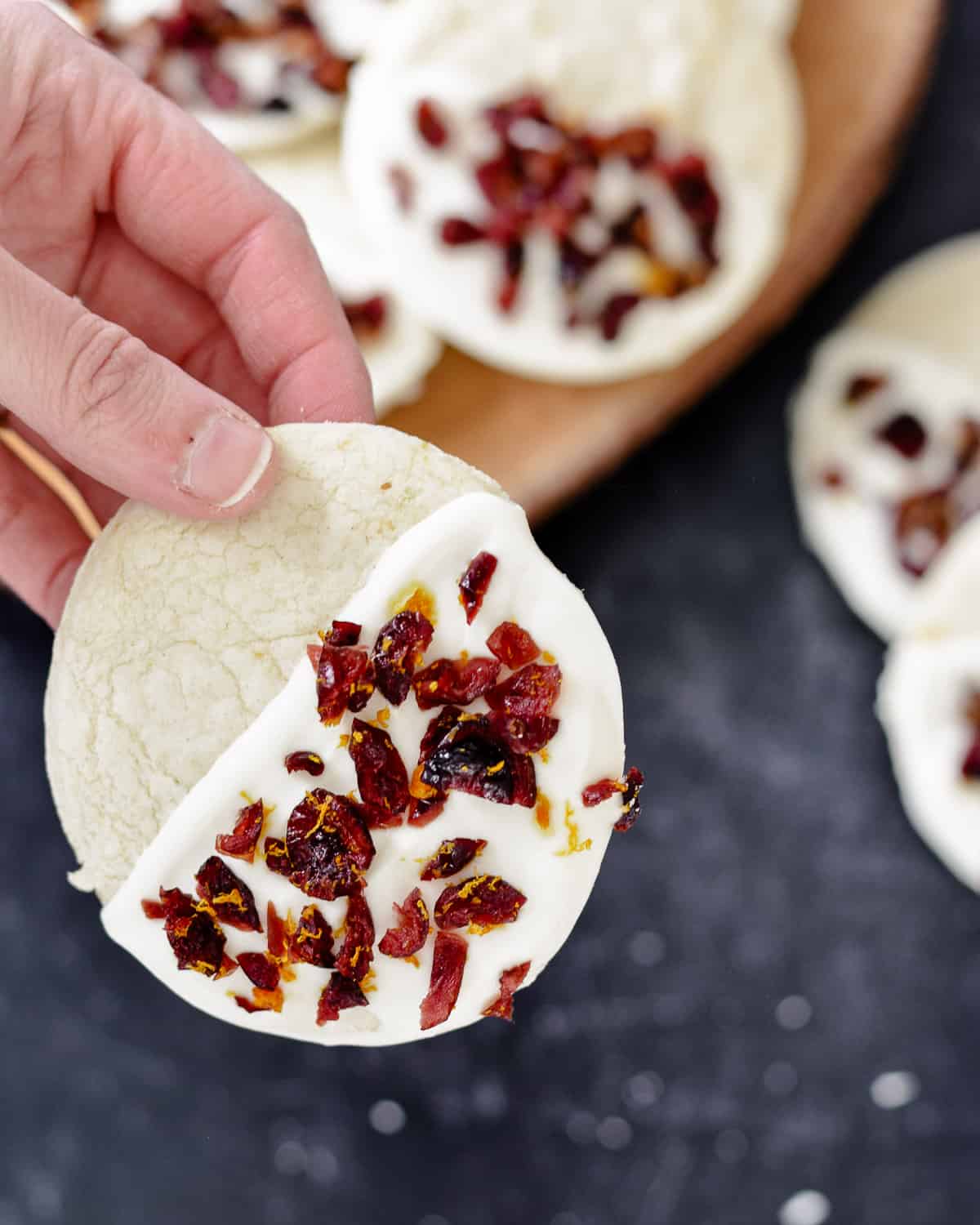 Hand holding up close of white chocolate dipped cookie with cranberry and orange zest.