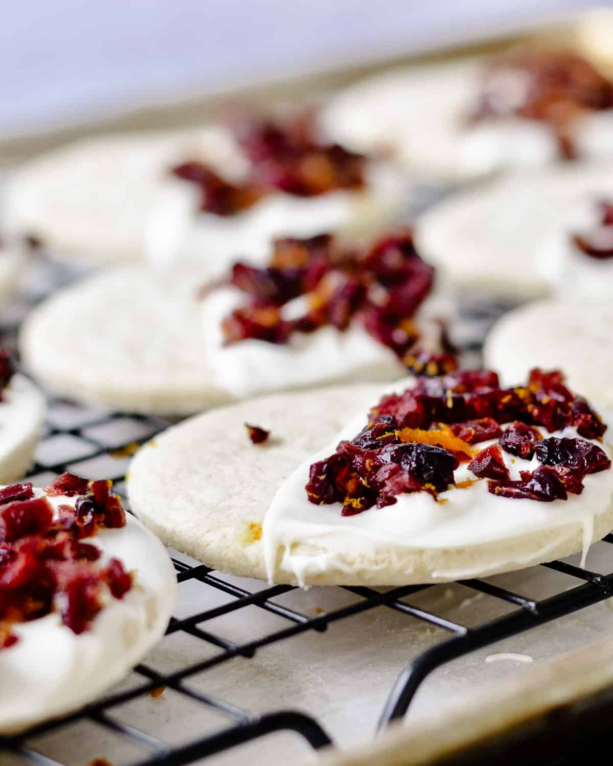 Close up of dried cranberry on top of white chocolate on top of cookie on a cooling rack.