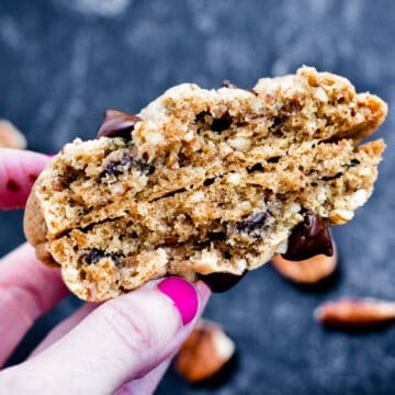 Hand holding a broken chocolate chip and pecan cookie.