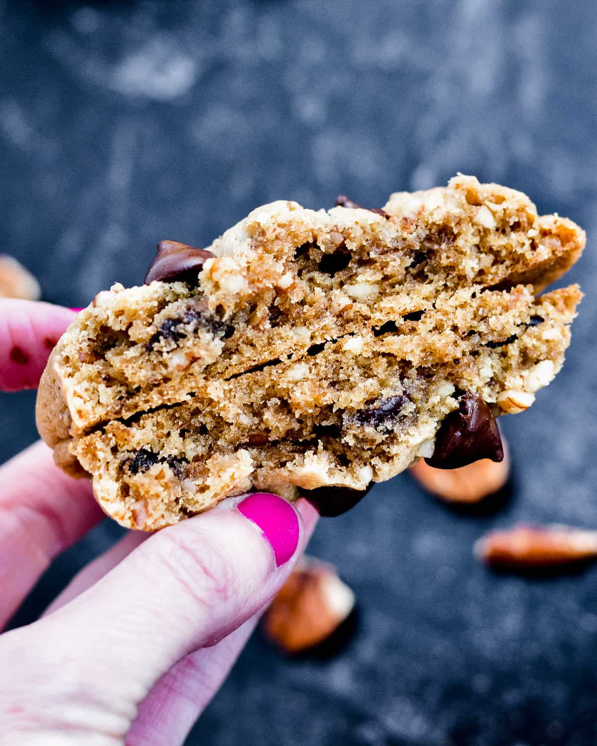 Hand holding a broken chocolate chip and pecan cookie.