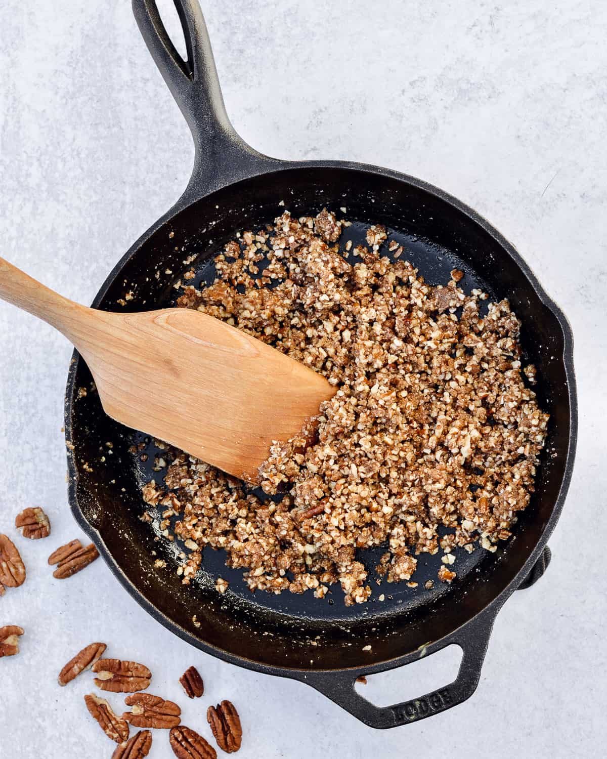 Cast iron skillet with chopped pecans and a wooden spatula.