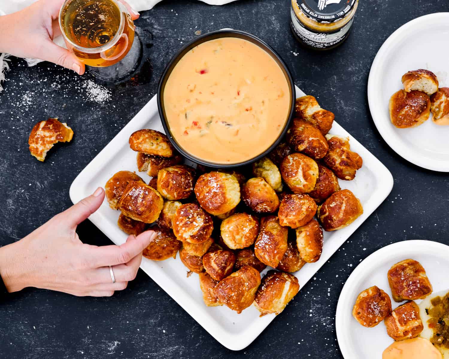 hand reaching for pretzel bite with queso dip on the side.
