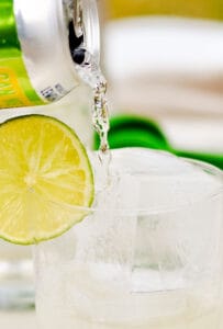 Seltzer water pouring into vodka and lime with a lime wede.