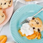 Large plate with chocolate chip shortcake cut open with peach sauce and whip cream on top. Another plate of shortcakes next to it.