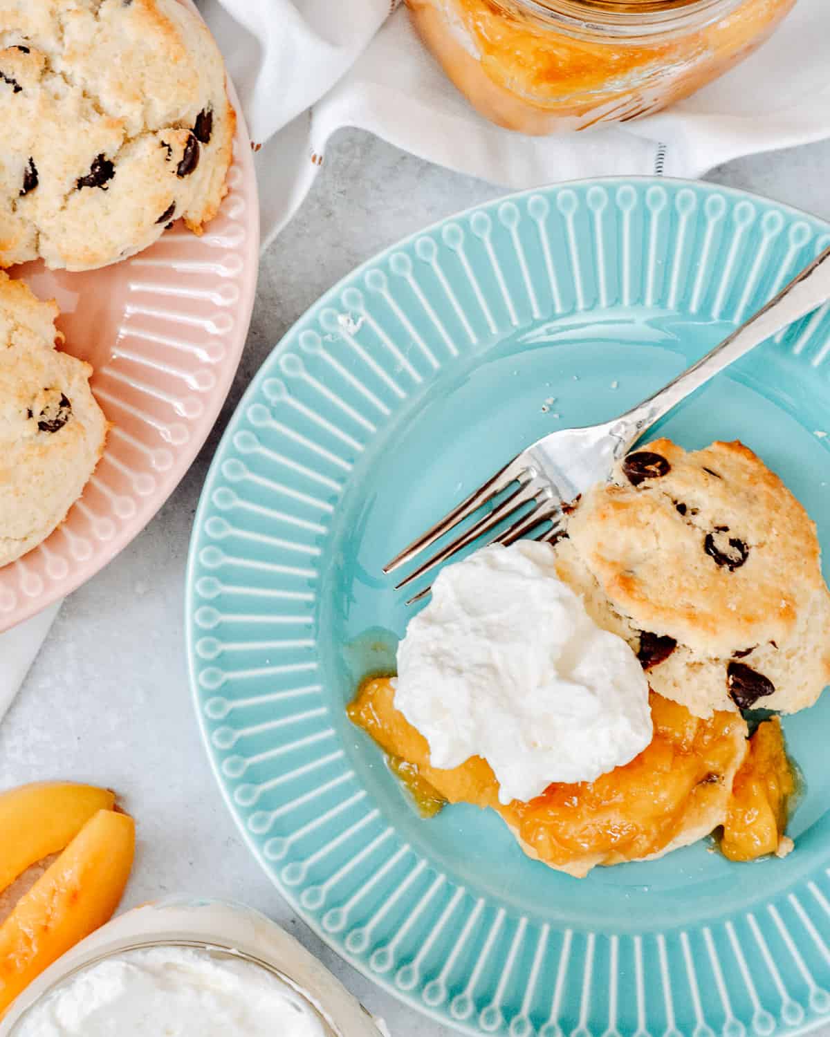 Large plate with chocolate chip shortcake cut open with peach sauce and whip cream on top. Another plate of shortcakes next to it.