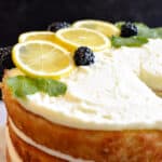 Close up of lemon layer cake topped with lemon slices, blackberries and mint leaves.