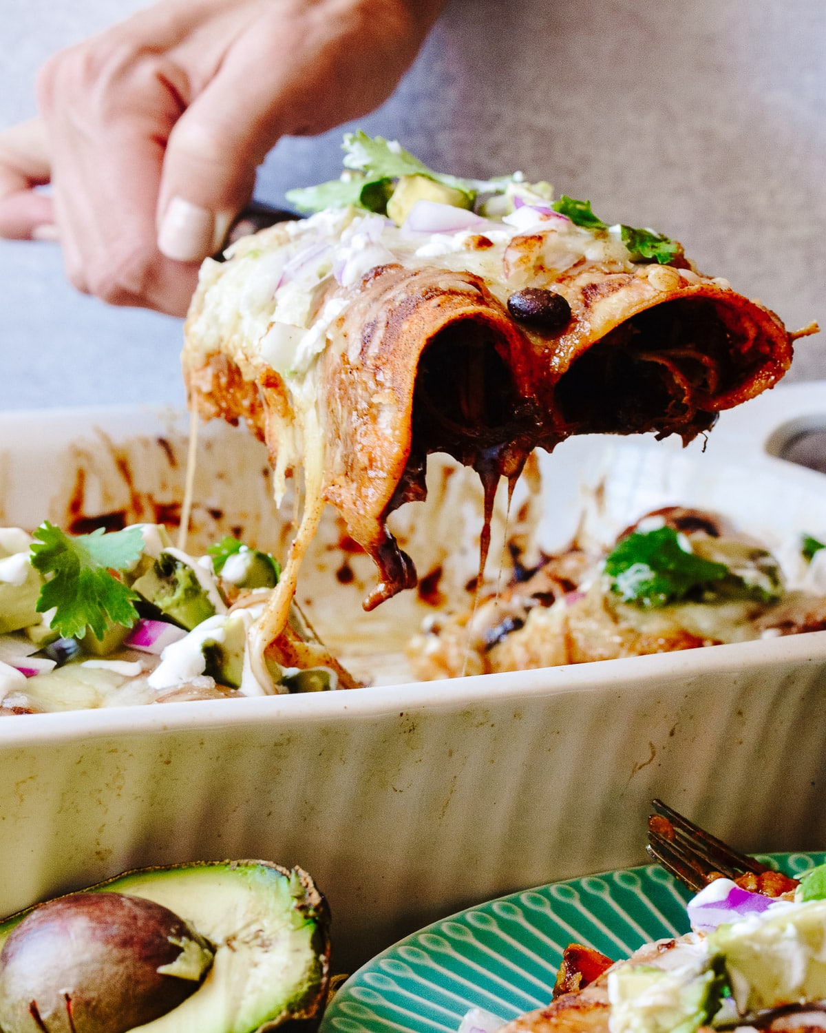Hand dishing up two enchiladas with toppings.