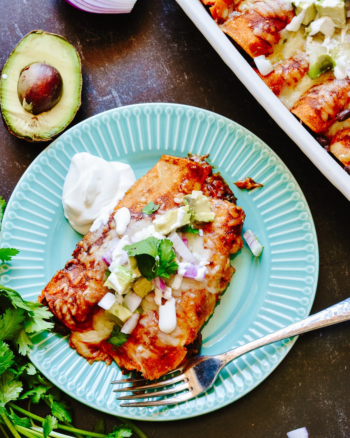 Enchiladas on a plate with a casserole dish beside with more enchiladas.