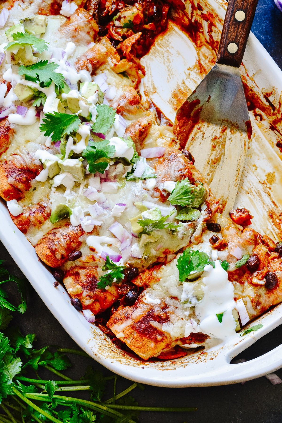 Half a dish of enchiladas with serving spatula.