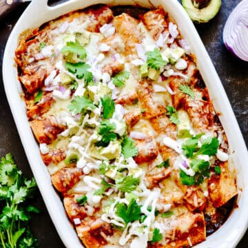 Dish of enchiladas with avocado and cilantro beside.