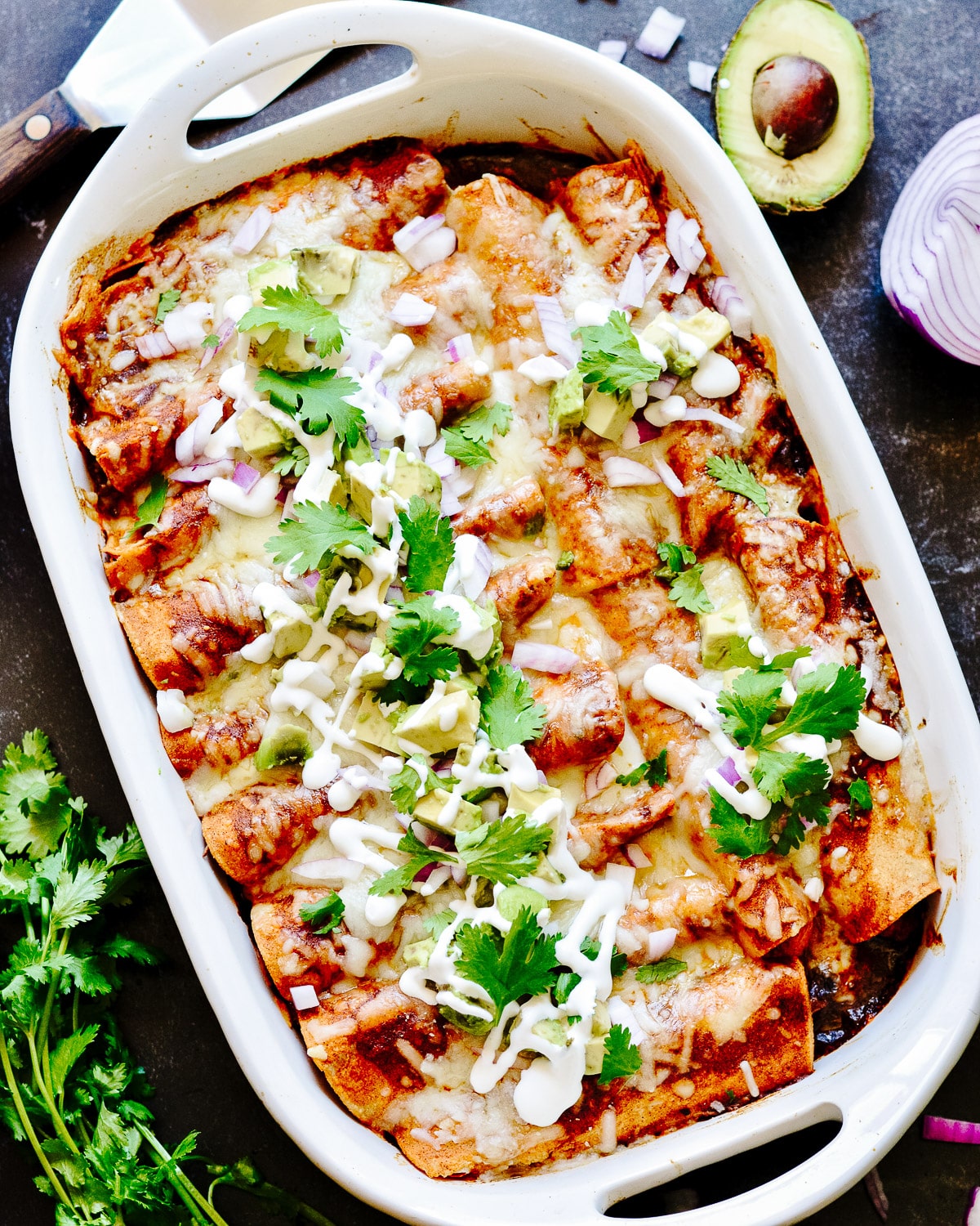 Dish of enchiladas with avocado and cilantro beside.