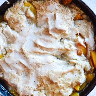 Cast Iron Peach Cobbler Perfection | Deliciously sweet fruit topped with a classic crisp biscuit topping. Add whip cream or ice cream and dig in! Perfect for parties.