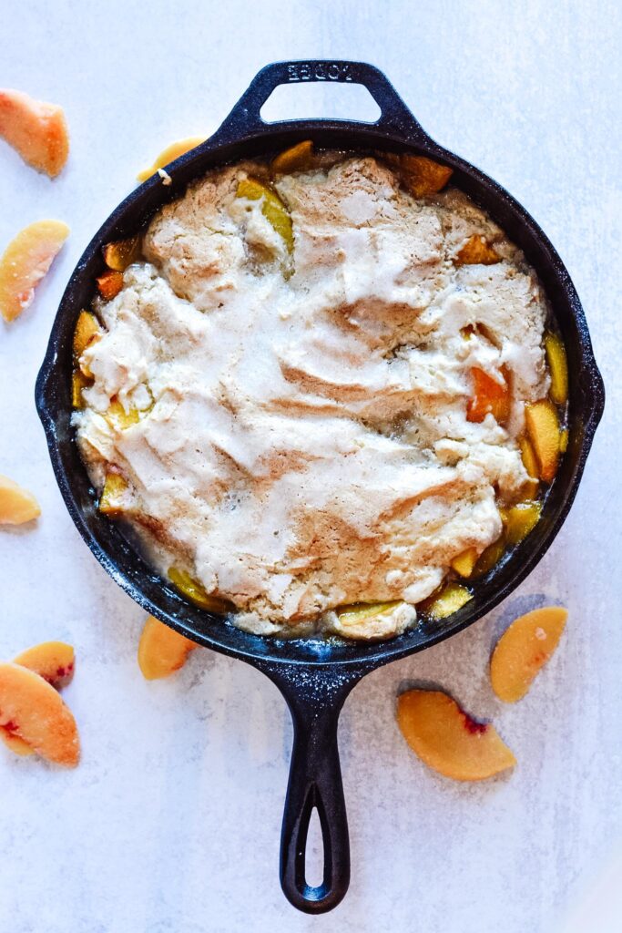 Cast Iron Peach Cobbler Perfection | Deliciously sweet fruit topped with a classic crisp biscuit topping. Add whip cream or ice cream and dig in! Perfect for parties.
