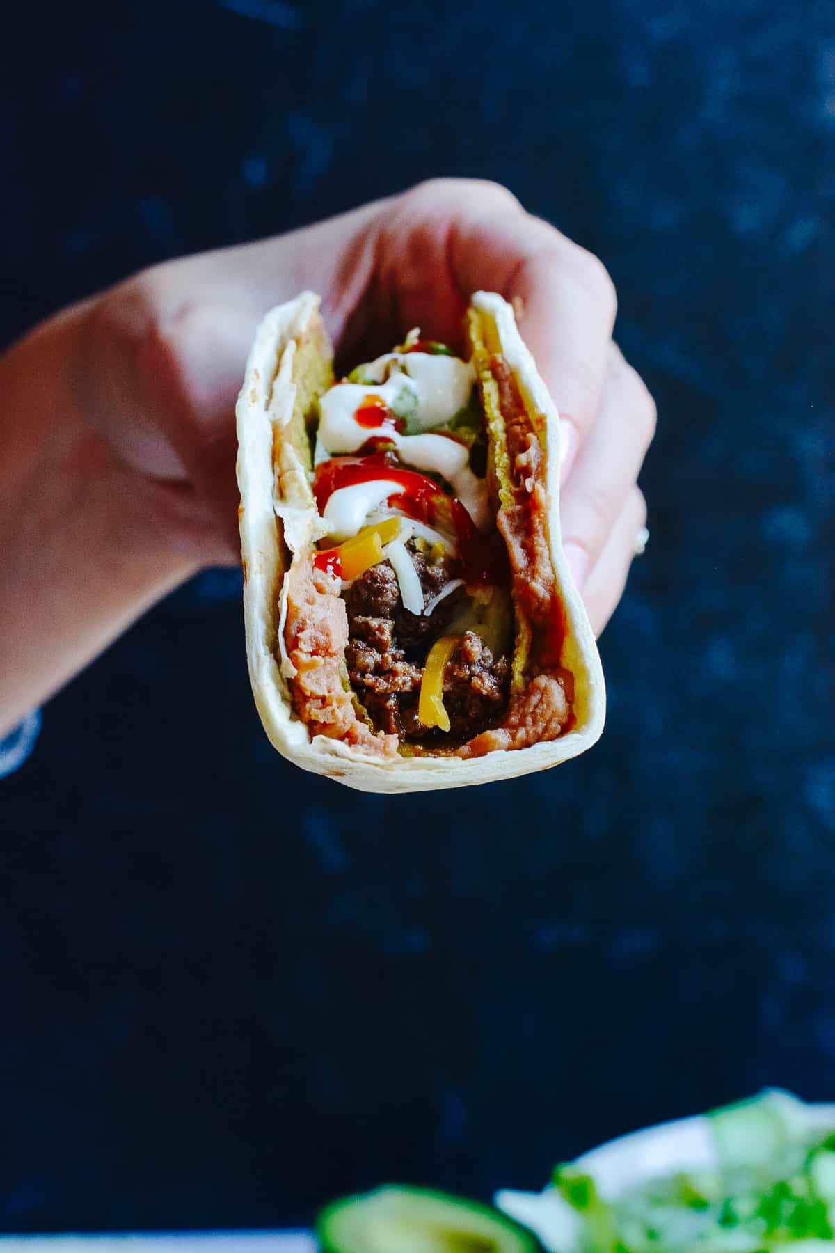 Hand holding a double decker taco with beef, beans and sauces.