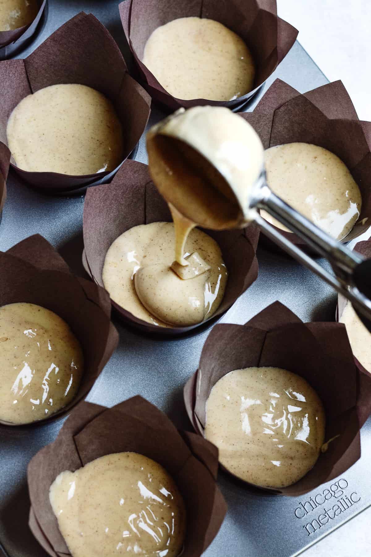 large scoop dropping cake batter into prepared cupcake tin with cupcake liners.