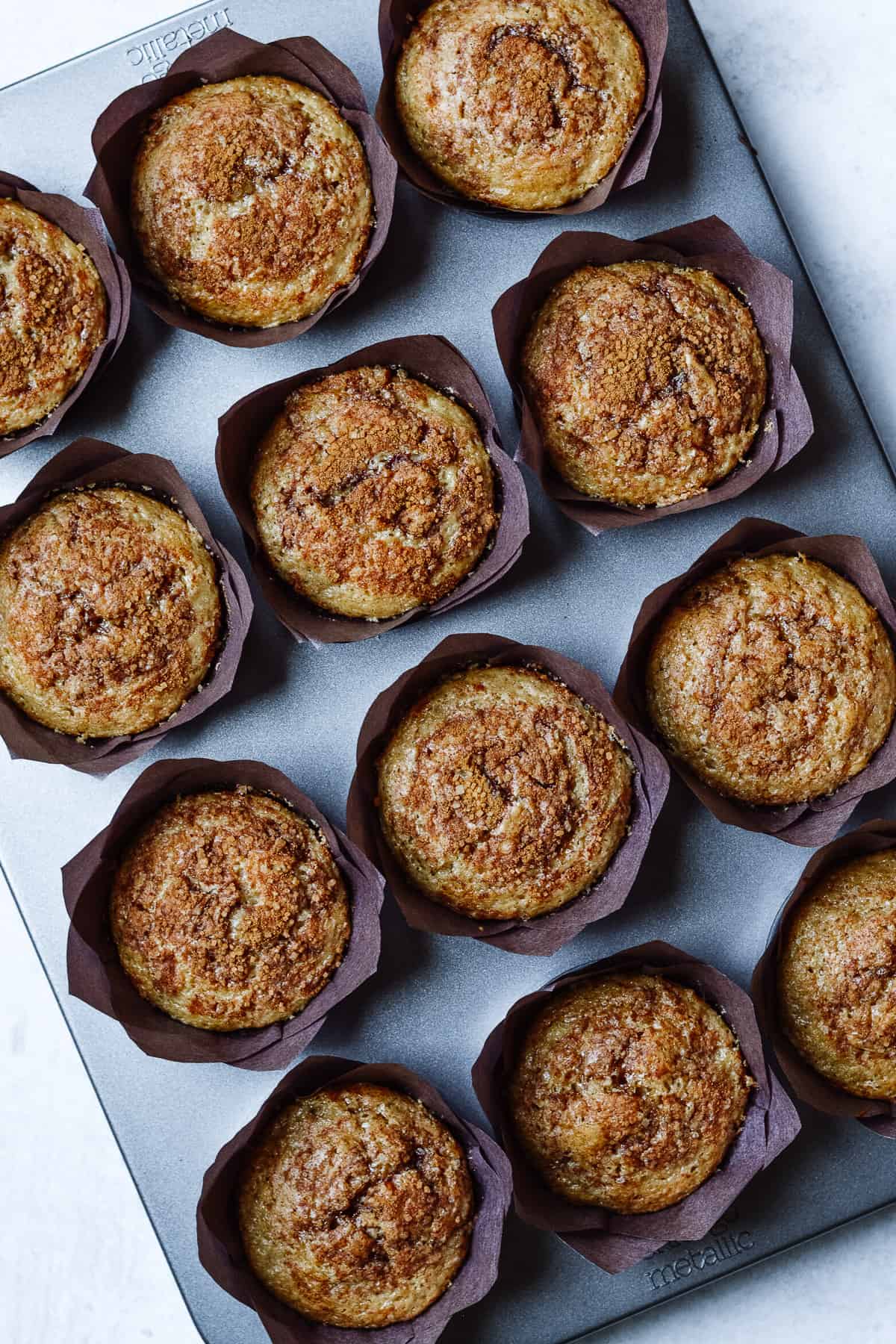 Baked cinnamon cupcakes in a cupcake pan with brown liners.