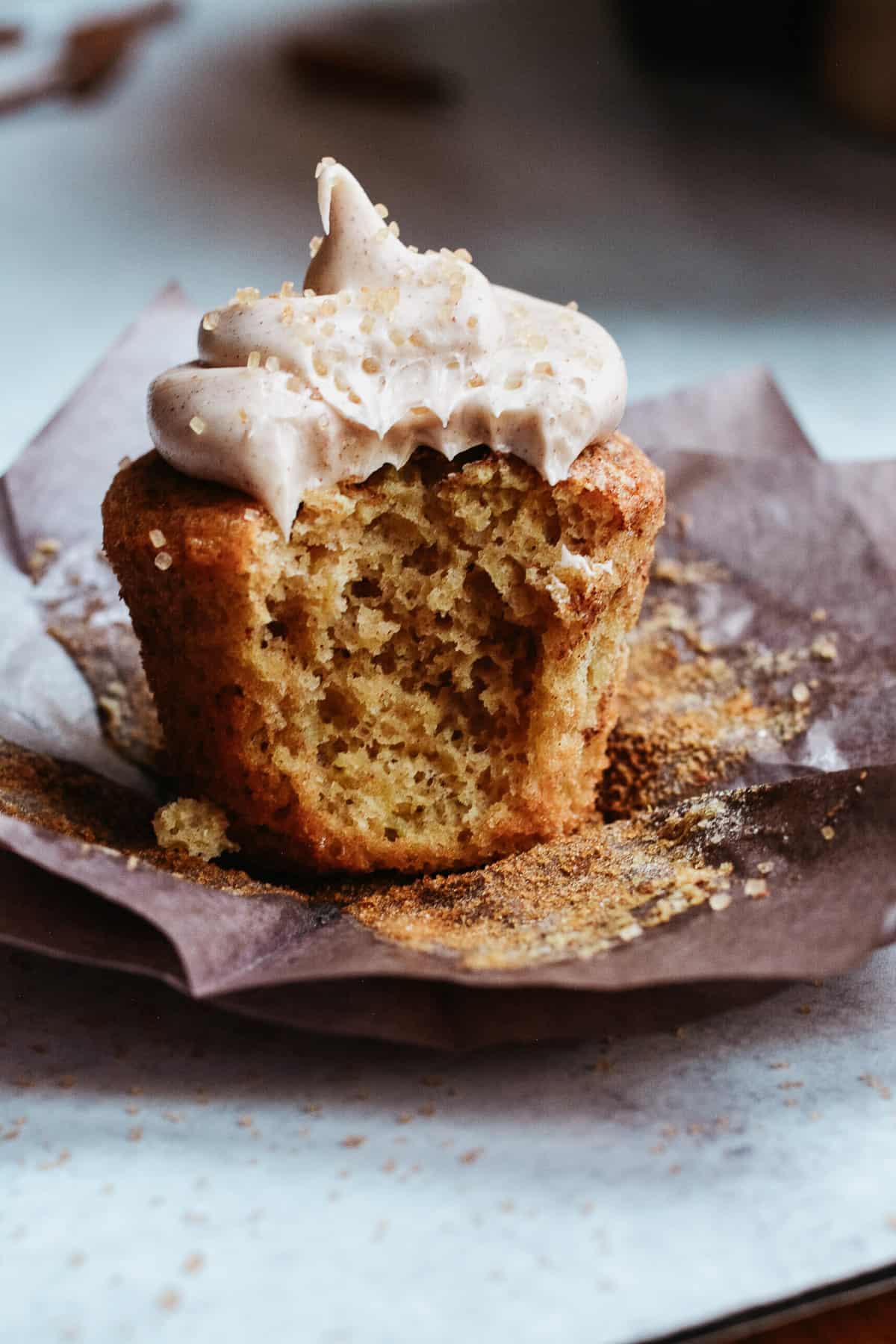 Bite out of a cupcake with frosting and sitting on a cupcake wrapper.