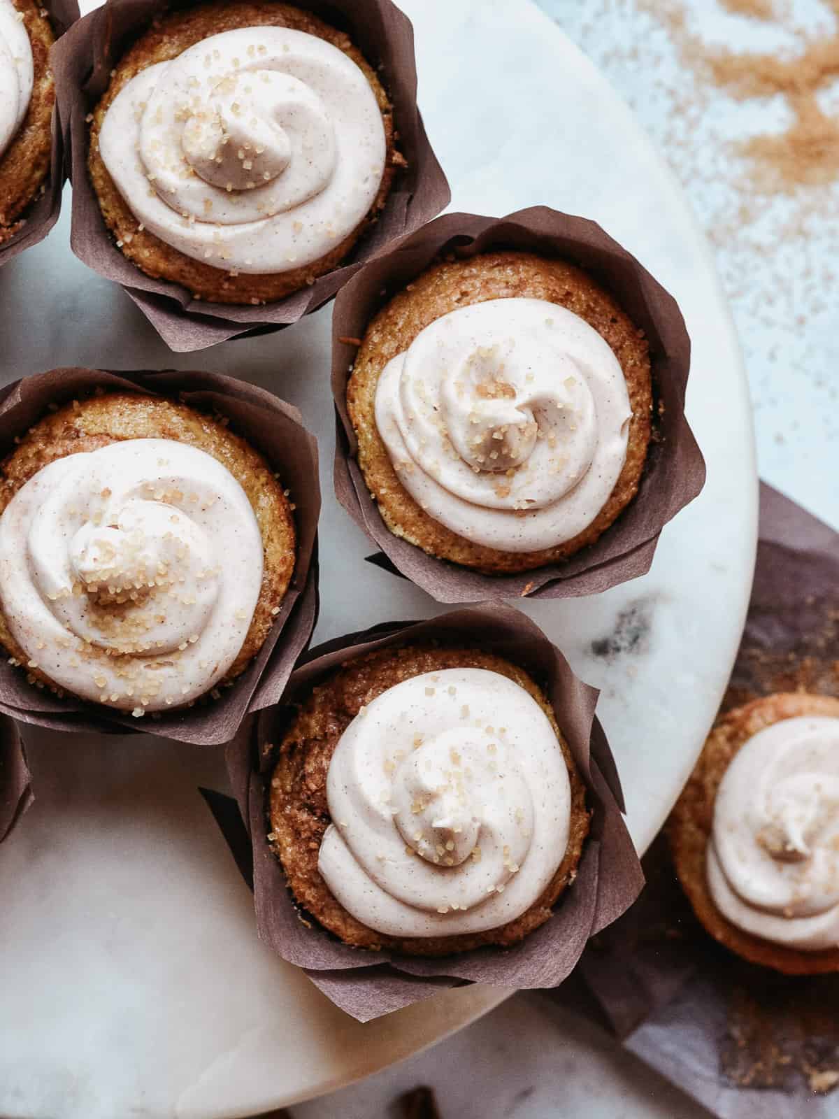 cinnamon cupcakes on a cake plate with sugar and cupcakes in the background.