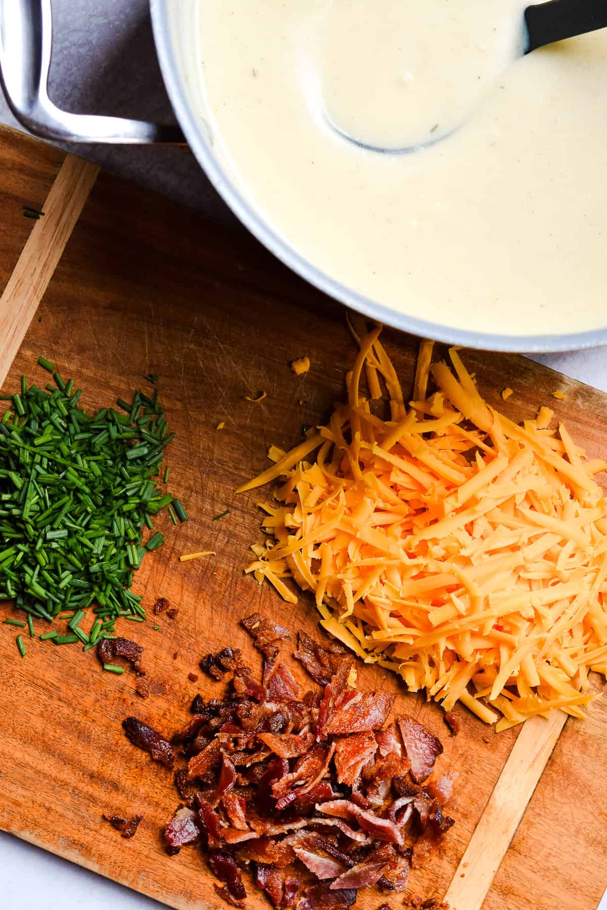 Pot of soup with shredded cheese, bacon and chives on the side.