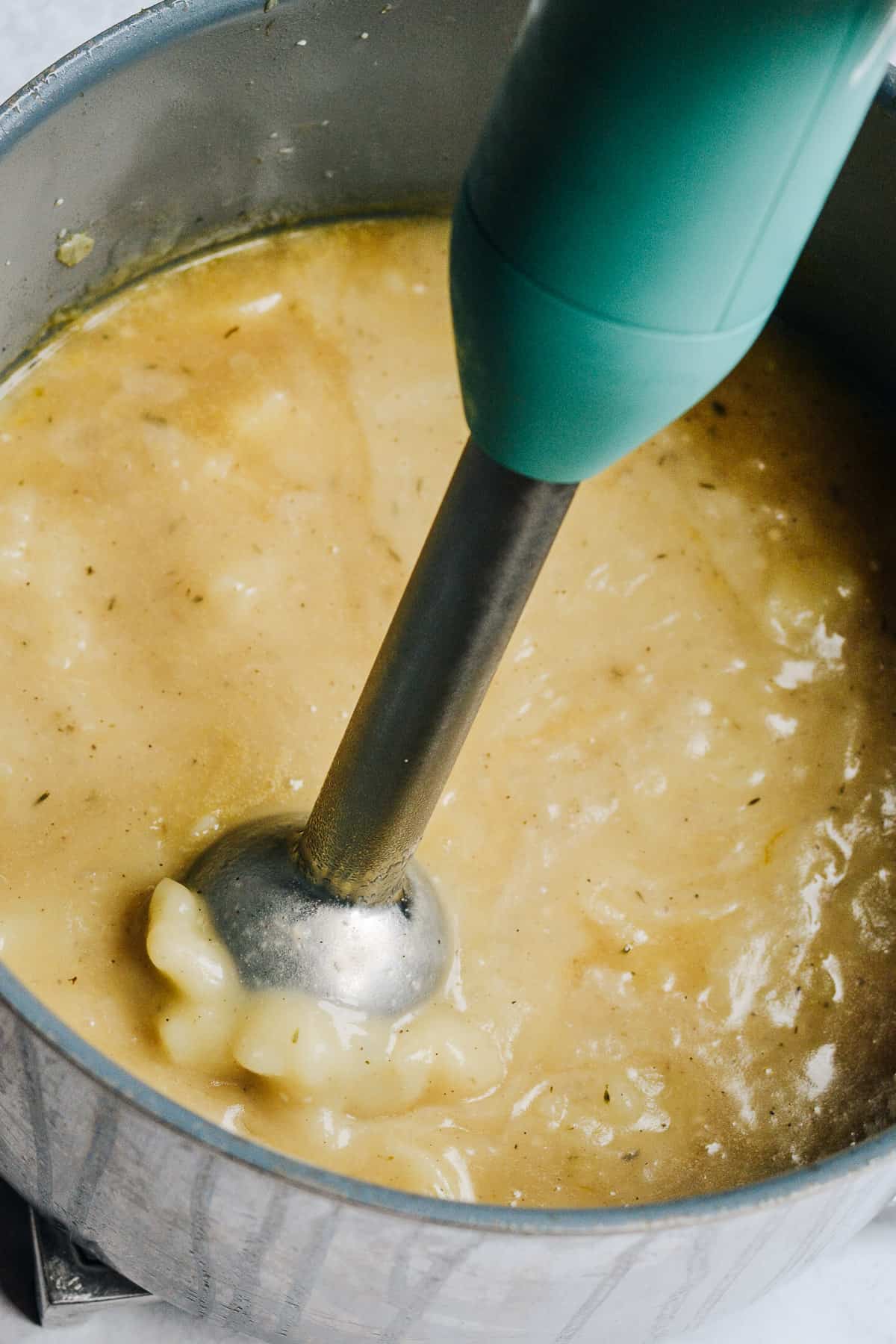 Hand blender blending the potatoes in soup in large pot.