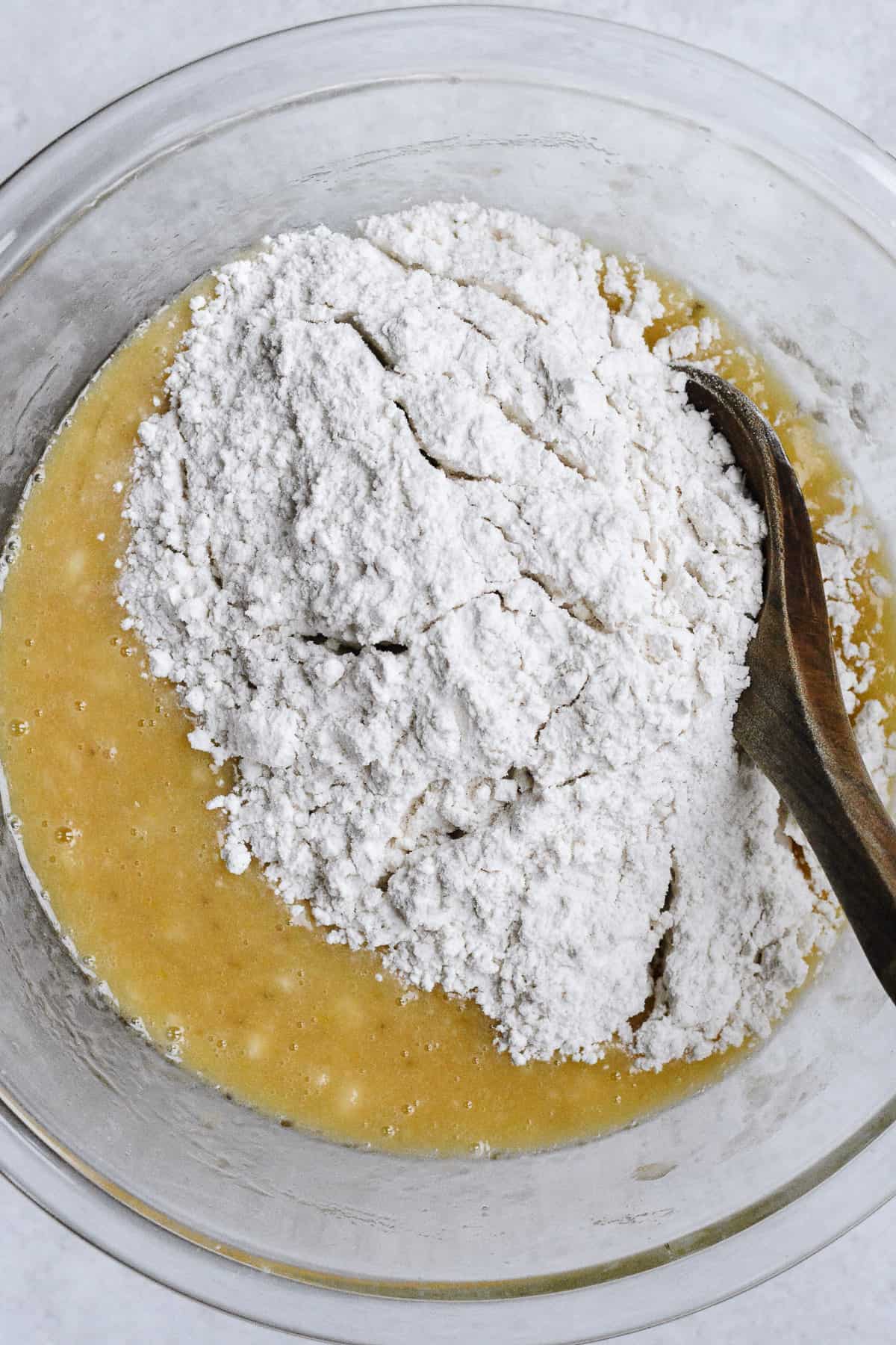 Flour blend added to wet blend with wooden spoon in bowl.