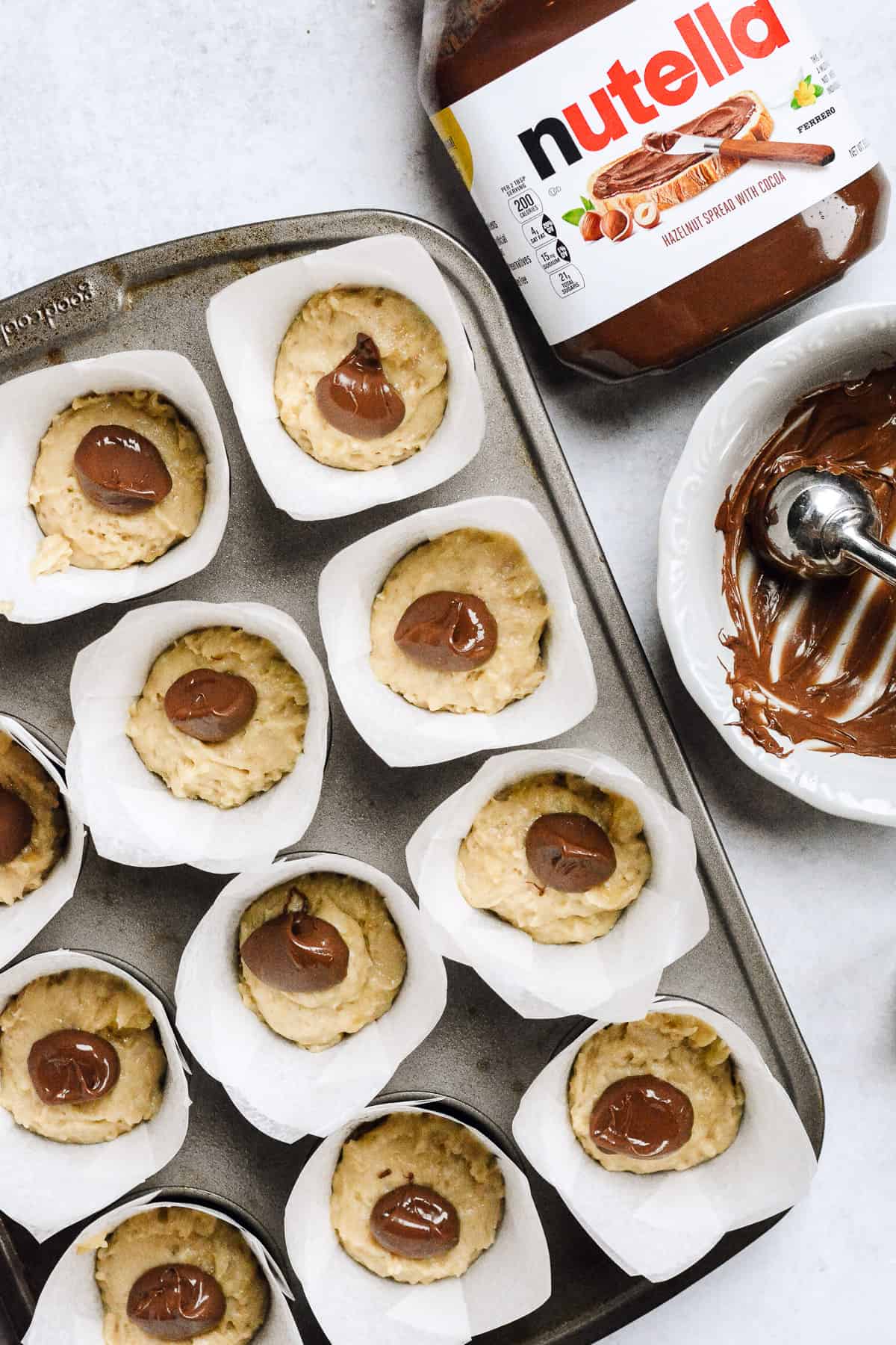 Nutella on top of banana muffin batter with nutella container on side.