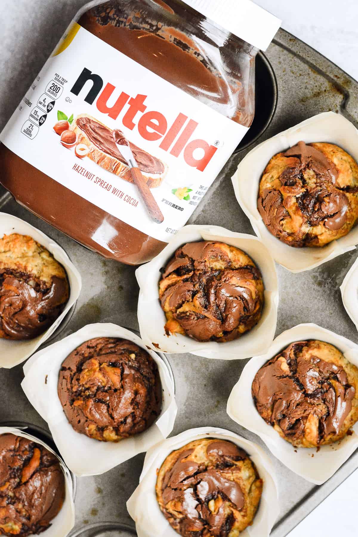 Nutella container next to nutella banana muffins in muffin tin.