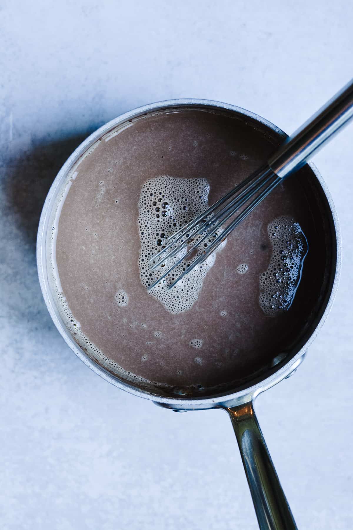Hot chocolate ingredients in a small saucepan with a wire whisk.