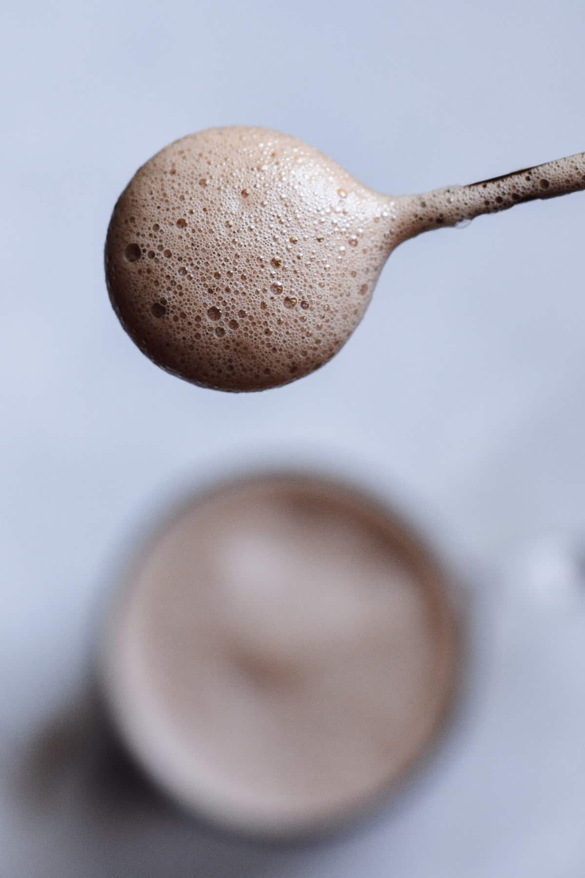 frothy milk on a spoon with the hot chocolate in the background.